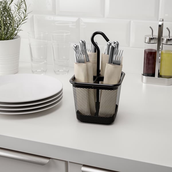 Black mesh cutlery caddy with handle on kitchen counter, holding silverware in four compartments.