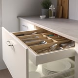 Open kitchen drawer with utensil organizer: knives, forks, spoons, and utensils neatly divided.