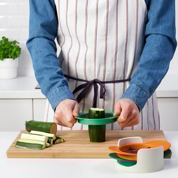 Person prepares zucchini using a colorful kitchen gadget, which slices fruits and vegetables efficiently.