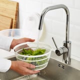Person washing lettuce in white strainer under modern chrome faucet in kitchen sink.