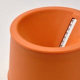 A close-up of a bright orange UPPFYLLD vegetable slicer, its smooth texture and sturdy design evident, with a glint of the steel blade visible.