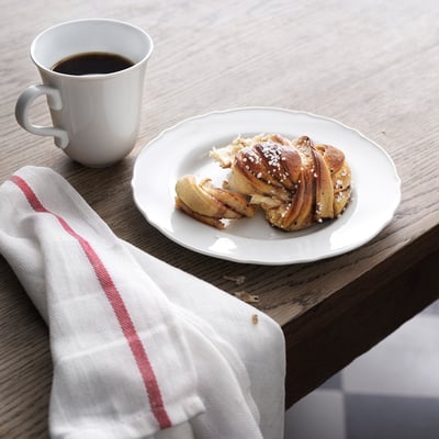 A rustic design white mug and plate set on a wooden table, with a pastry on the plate and coffee in the mug.