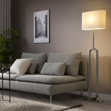 An UPPVIND floor lamp with a slim, oval shade, standing tall beside a grey sofa, casting a warm glow.