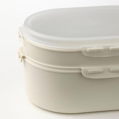 A white, oval-shaped, two-tiered plastic lunch box with a clear lid, designed for stacking and separating food items.