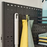 Organized cleaning supplies on hooks and shelves. Includes a brush, yellow cloth, green cloth, and stack of cloths, mounted on a pegboard panel.