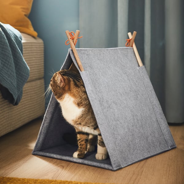 Cat inside grey felt tent house, looking out. Part of UTSÅDD series for pet comfort and relaxation.