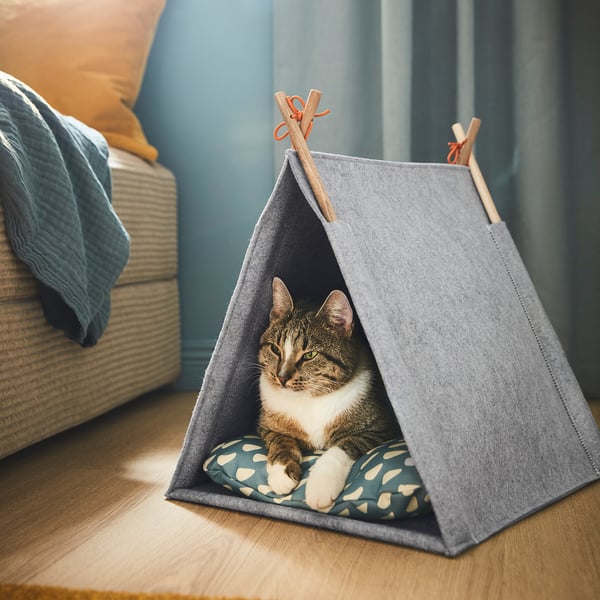 A cat lounges inside a small, grey felt tent, likely a cozy cat house, on a wooden floor.