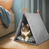 A cat lounges inside a small, grey felt tent, likely a cozy cat house, on a wooden floor.