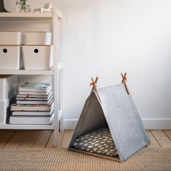 Small grey cat tent, UTSÅDD, on rug beside white shelves with books & boxes.