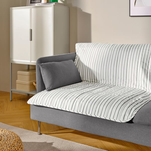 Striped sofa with one gray pillow, atop wooden floor. Beside white cabinet with stacked boxes.