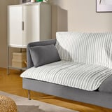 Striped sofa with one gray pillow, atop wooden floor. Beside white cabinet with stacked boxes.
