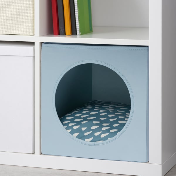 A light blue pet cushion with a circular opening for cats or small dogs, placed on a white shelf.