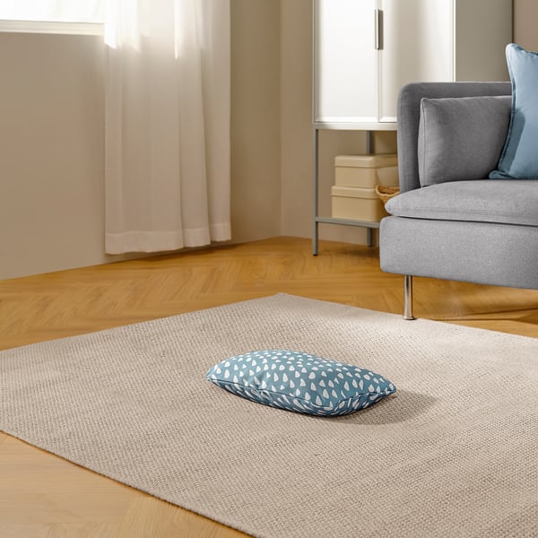 A cozy pet cushion on a rug near a grey armchair, perfect for cats or small dogs to relax and sleep.