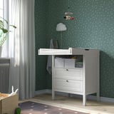 Baby changing station with drawers, hanging mobile, and toys, set against an patterned wallpaper.