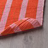 Bright orange and white striped door mat with textured surface, designed to welcome and enhance entryways, laid on wooden floor.