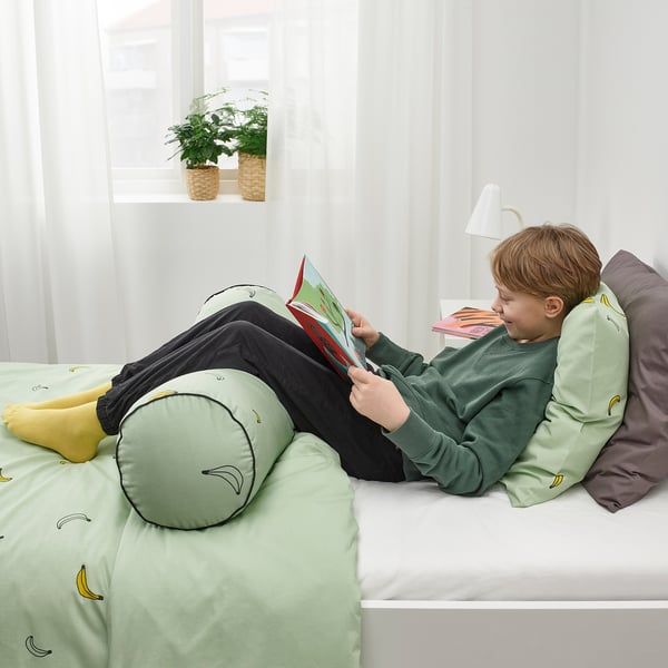 A boy reads on a bed with a green VÄNKRETS support pillow.