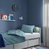 Small, white bed with blue banana-patterned sheets. Under-bed storage, serves as kids furniture.