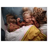 Two children sleeping, one holding a leopard pillow, under a yellow blanket, wearing matching brown pajamas with dark spots.