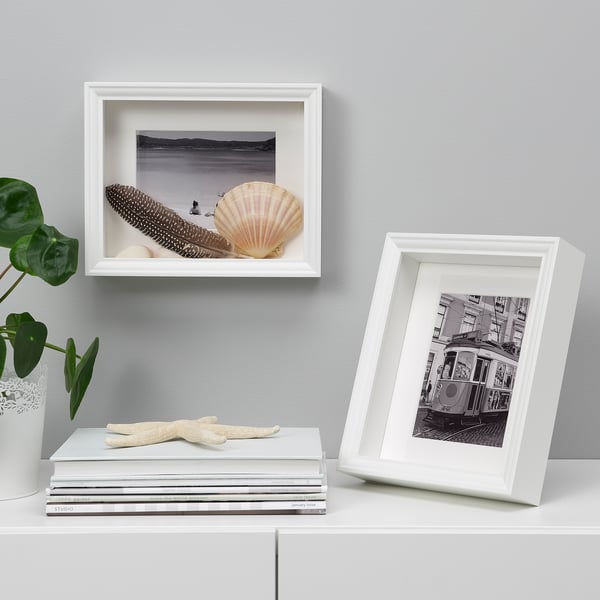 White frames display photos and a seashell. One stands, one hangs, with a plant and starfish nearby.