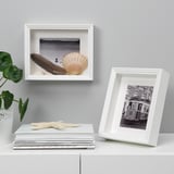 White frames display photos and a seashell. One stands, one hangs, with a plant and starfish nearby.