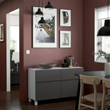 Modern dining room with VÄSTERVIKEN sideboard, art, dark red wall, black lamps, and wooden chairs.