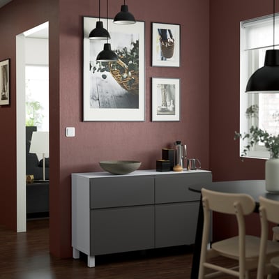 Modern dining room with VÄSTERVIKEN sideboard, art, dark red wall, black lamps, and wooden chairs.