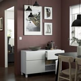 Modern dining area with white storage unit featuring integrated handles and open drawer. Decorative bowl, cups, and art on dark purple wall.