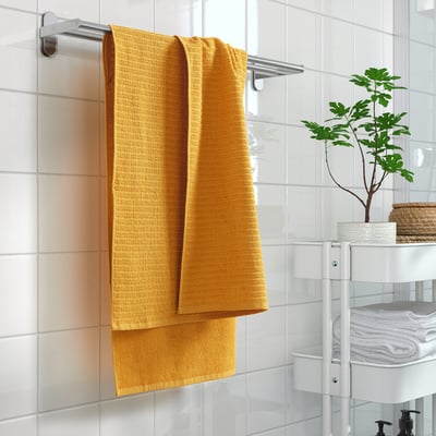 Yellow towel on metal rack, white wall, with plant.