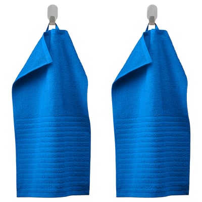 Two blue VÅGSJÖN towels hang side by side on silver hooks, displaying solid terry texture and striped lower half design in vibrant blue.