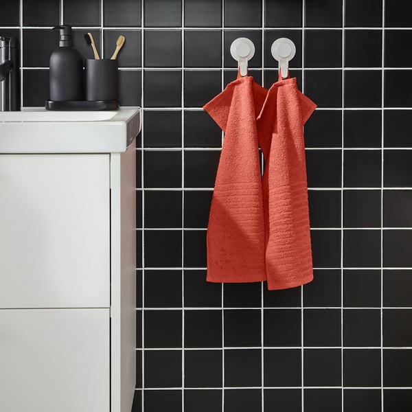Red VÅGSJÖN towels hang on black-tiled wall, white sink left.
