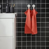 Red VÅGSJÖN towels hang on black-tiled wall, white sink left.