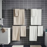 Modern bathroom with dark gray tiled walls. Four towels hang neatly in rows, two beige and two white, on silver towel rails.