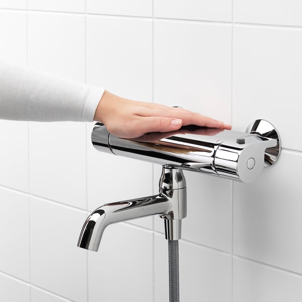 Person adjusts chrome bathroom faucet, featuring temperature control and safety stop button.