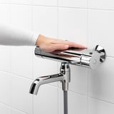 Person adjusts chrome bathroom faucet, featuring temperature control and safety stop button.