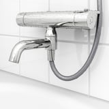 Close-up of chrome shower mixer with braided hose, featuring adjustable spout and temperature safety button.