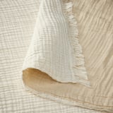 Soft, crinkled cotton throw with raw edges, folded on cream backdrop.