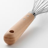 Wooden-handled whisk with stainless steel loops, designed for efficient mixing, resting on a white surface.