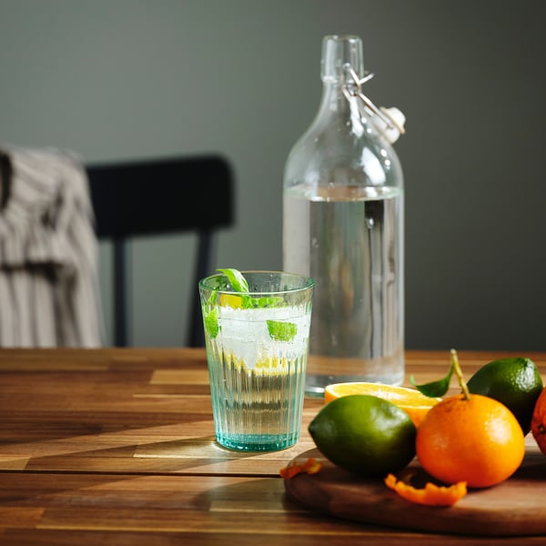 A glass filled with water and mint on a wooden table, with a bottle and fruits nearby.