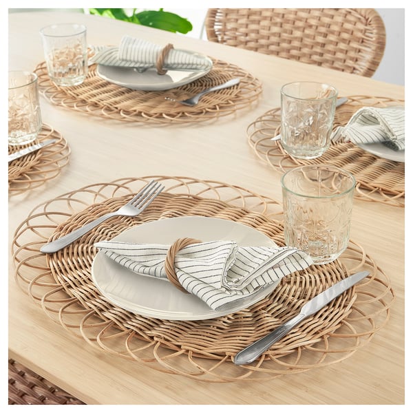 Four woven rattan place settings on table, including plates, cutlery, napkins, and glasses.