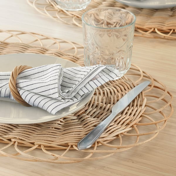 A dining table set with wicker placemats, white plates, folded striped napkins, a knife, and a glass, showcasing a rustic, handwoven design.