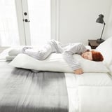 Woman resting on side with long body pillow on bed.