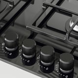 Black gas stove with four knobs, cast iron supports, glass surface. Advanced safety and control for precise cooking.