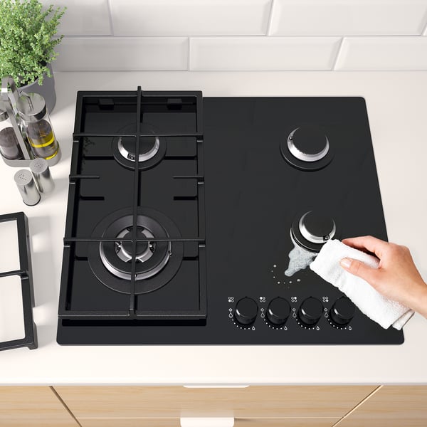 A modern kitchen scene showing a person cleaning a gas hob with five burners and cast iron supports for safety and precision cooking.