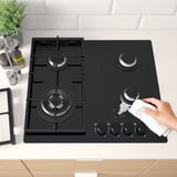 A modern kitchen scene showing a person cleaning a gas hob with five burners and cast iron supports for safety and precision cooking.