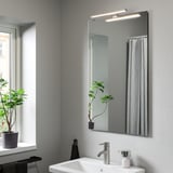 Modern bathroom with VÅTHULT wall lamp, sleek design, above sink.