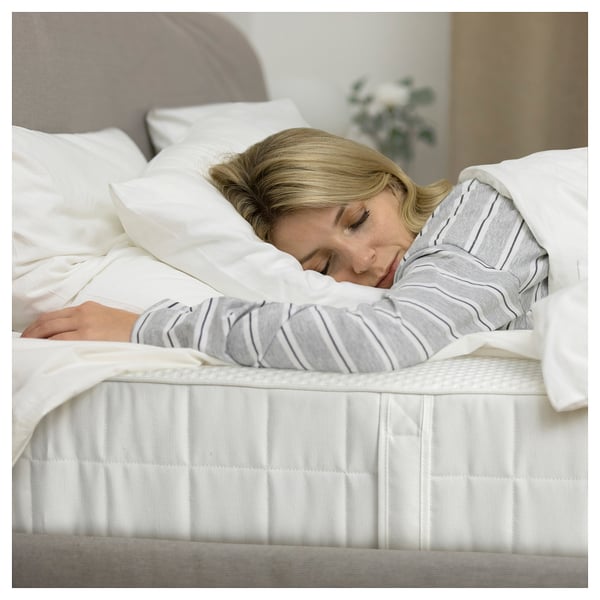 Person sleeping on white mattress with pillows in calm, softly lit room.