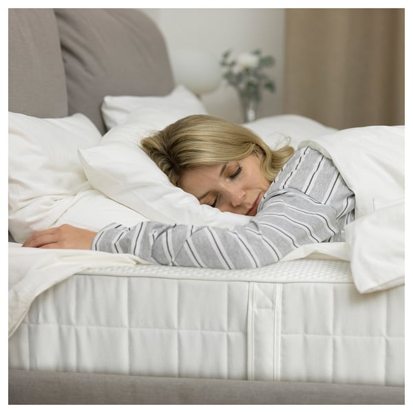 Sleeping on vattyo mattress, white linens, grey shirt. Pillow, vase with flowers.
