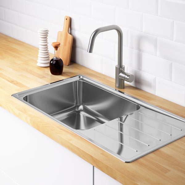 Stainless steel sink with drainboard and faucet on wooden countertop.