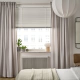 Modern bedroom with large VECKLARFLY blinds, light gray, covering wide window, matching curtains, potted plants, and a cozy bed.