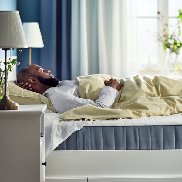 Man resting on comfortable vesteroy mattress in serene bedroom with light blue curtains.